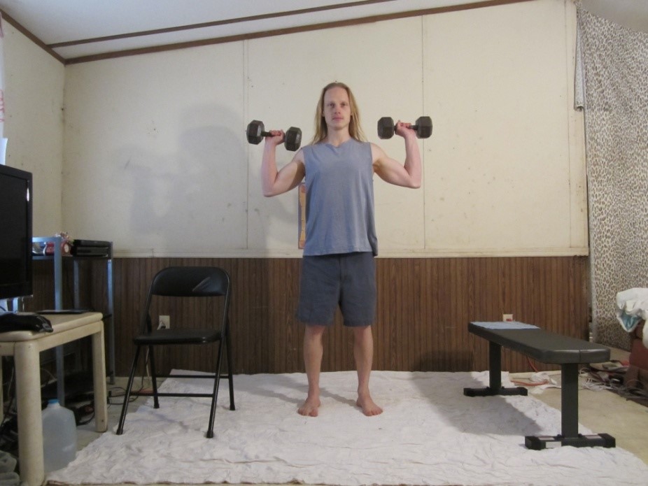 Dumbbell standing shoulder press picture demonstrating the beginning of the repetition from a front viewpoint.