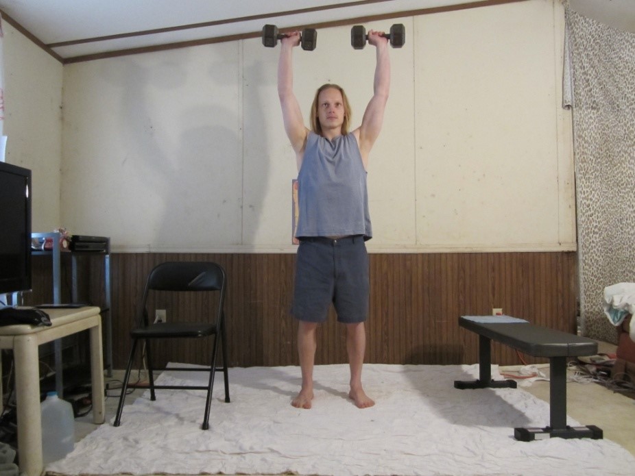 Dumbbell standing shoulder press picture demonstrating the middle of the repetition from a front viewpoint.